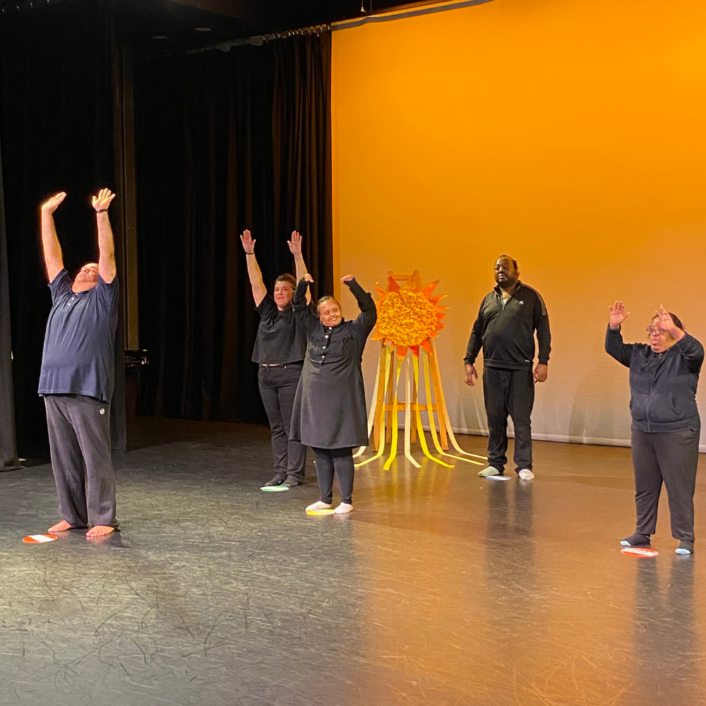A group of dancers stand on the stage with arms stretched up.