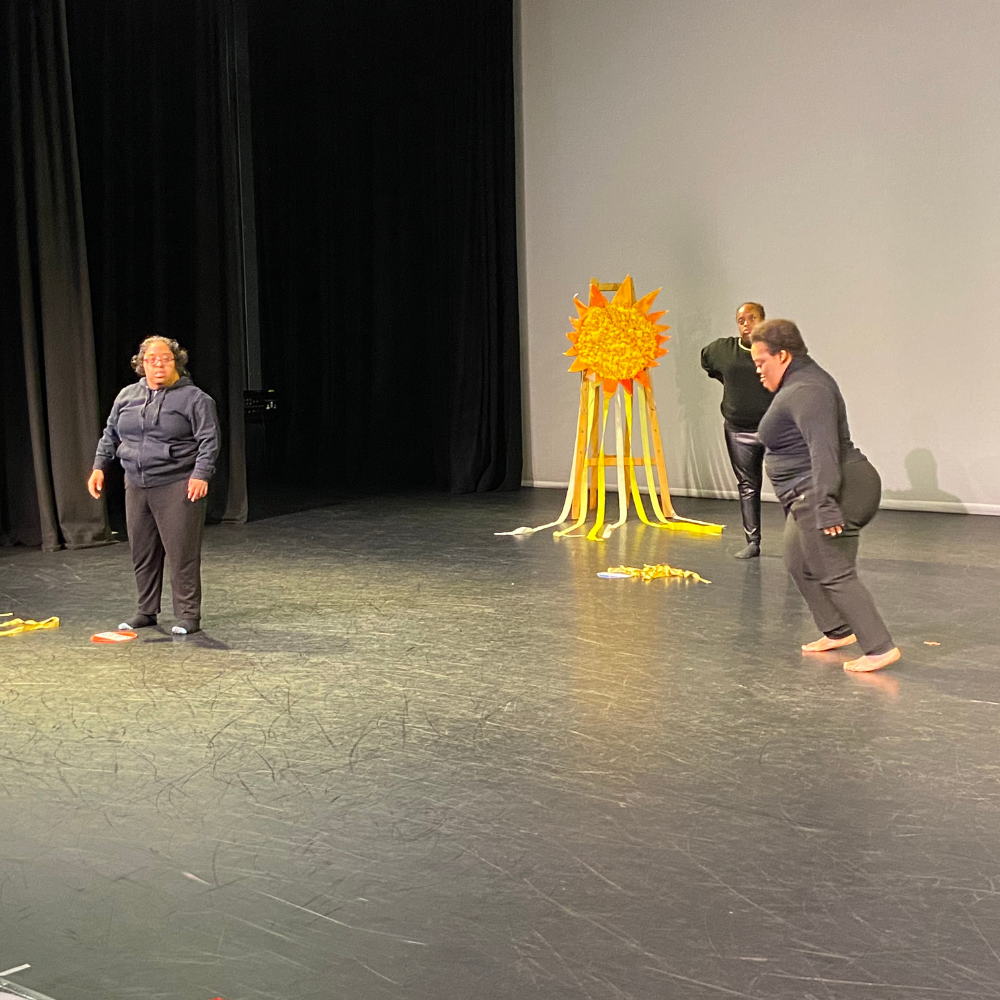 Dancers perform on stage, dancing around a paper sun