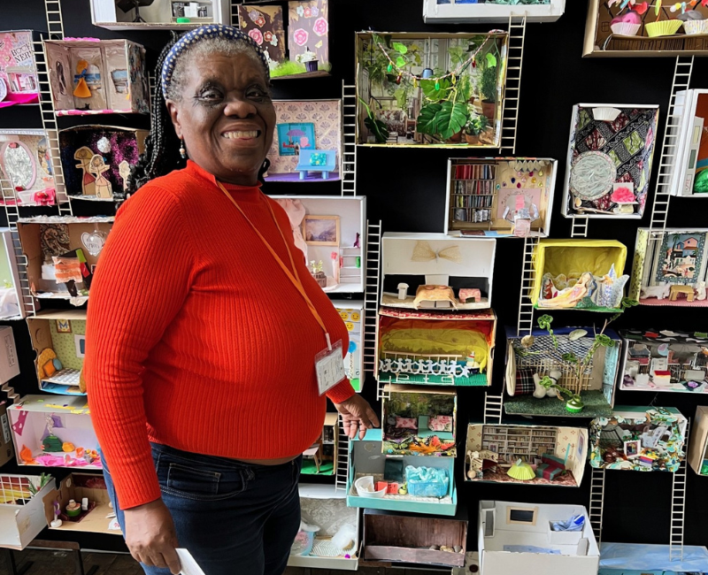 A lady stands smiling in front of the shoebox installation