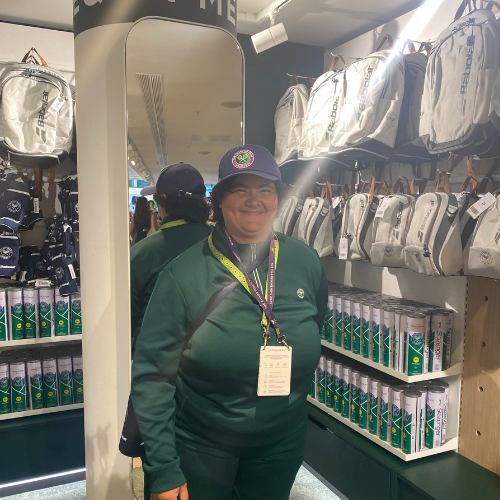 Charlotte stands smiling inside the shop at her job at Wimbledon