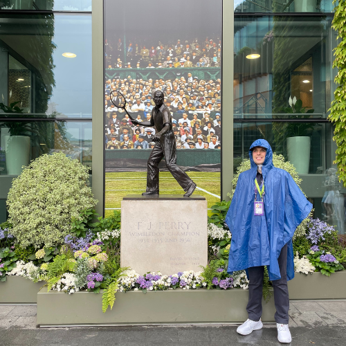 Joe stands in the rain in his raincoat next to the Fred Perry statue at Wimbledon