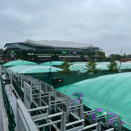 The inevitable rain at Wimbledon! Courts are shown in the rain with the green covers pulled over them under a grey sky.