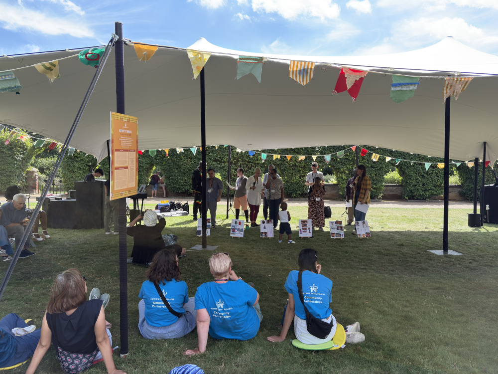 Audience members sit on the grass watching performers singing under a marquee