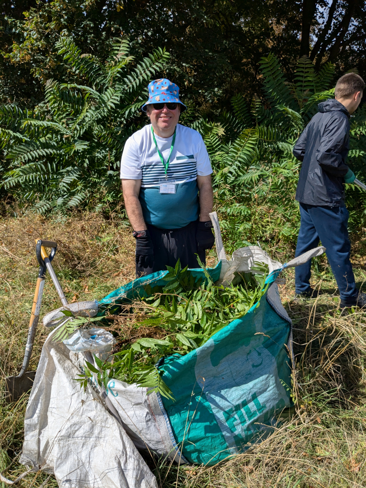 A man stands smiling in front of a big bag of garden foliage that has been removed from a tree