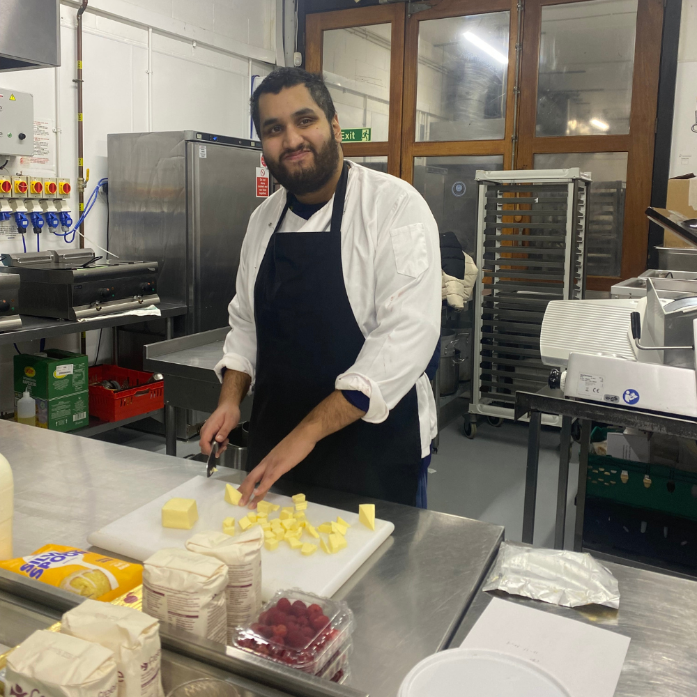 Share student Zain, a young man stands cutting up segments of butter to use in his scone recipe.