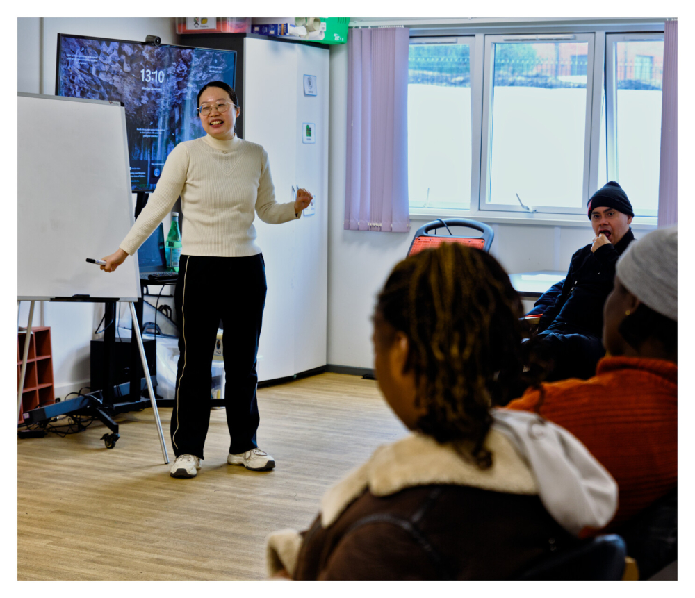 A lady running a workshop stands at the front of the class explaining something and writing on a flip chart