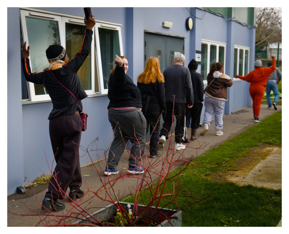 A group of people walk in single file one has her hands up in the air, it's part of a fun movement activity