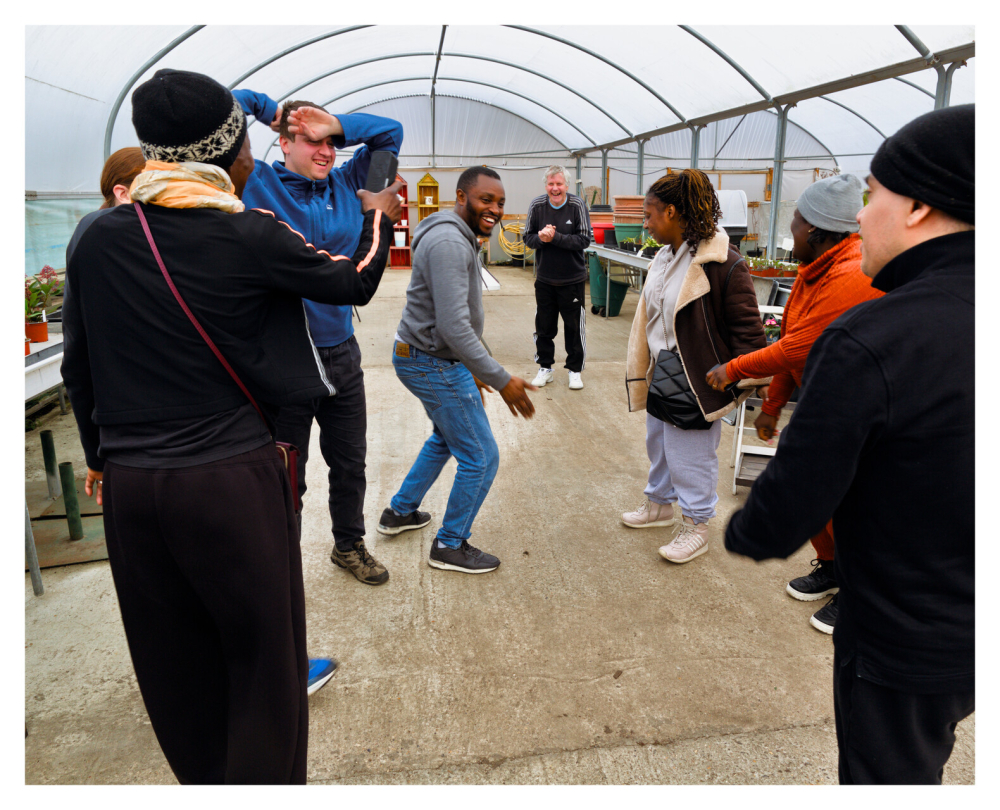 A group of people are moving in a polytunnel at Share's garden as part of a movement workshop