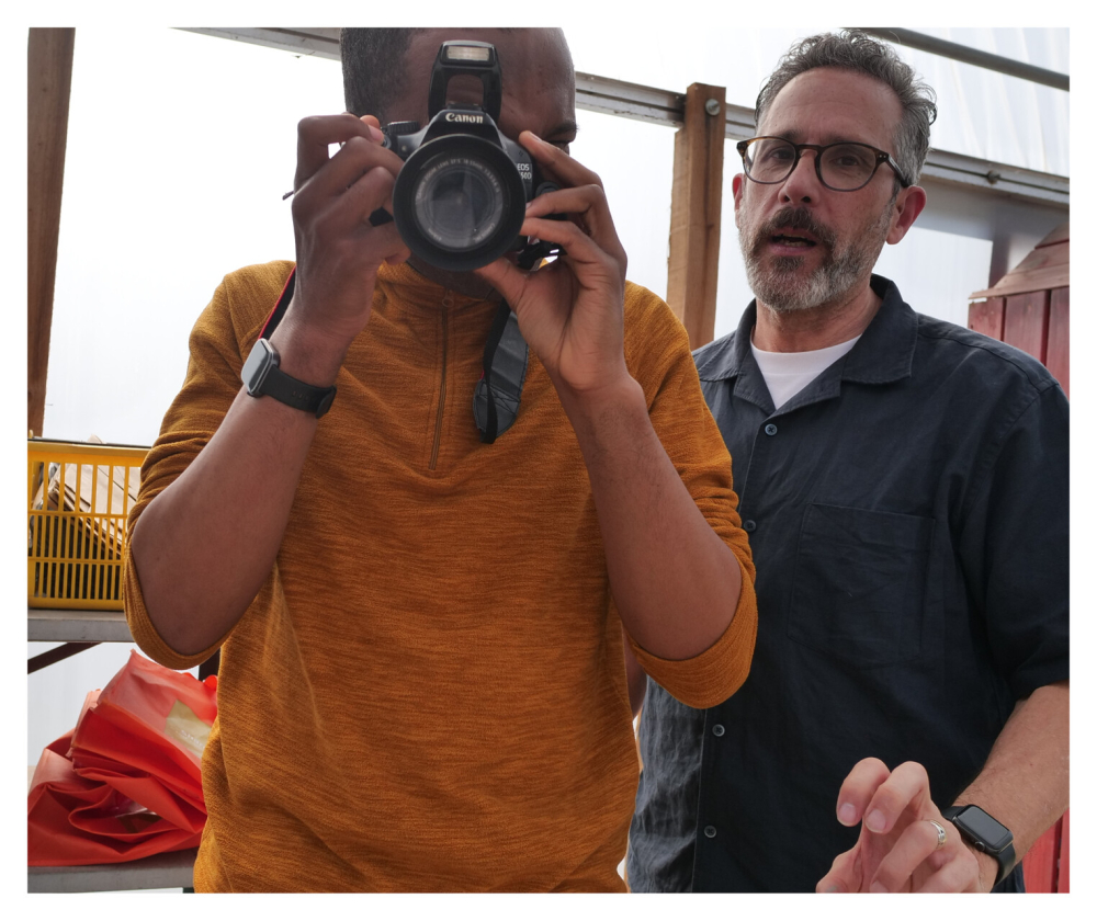 A man has a camera and is taking a photo with another man behind him
