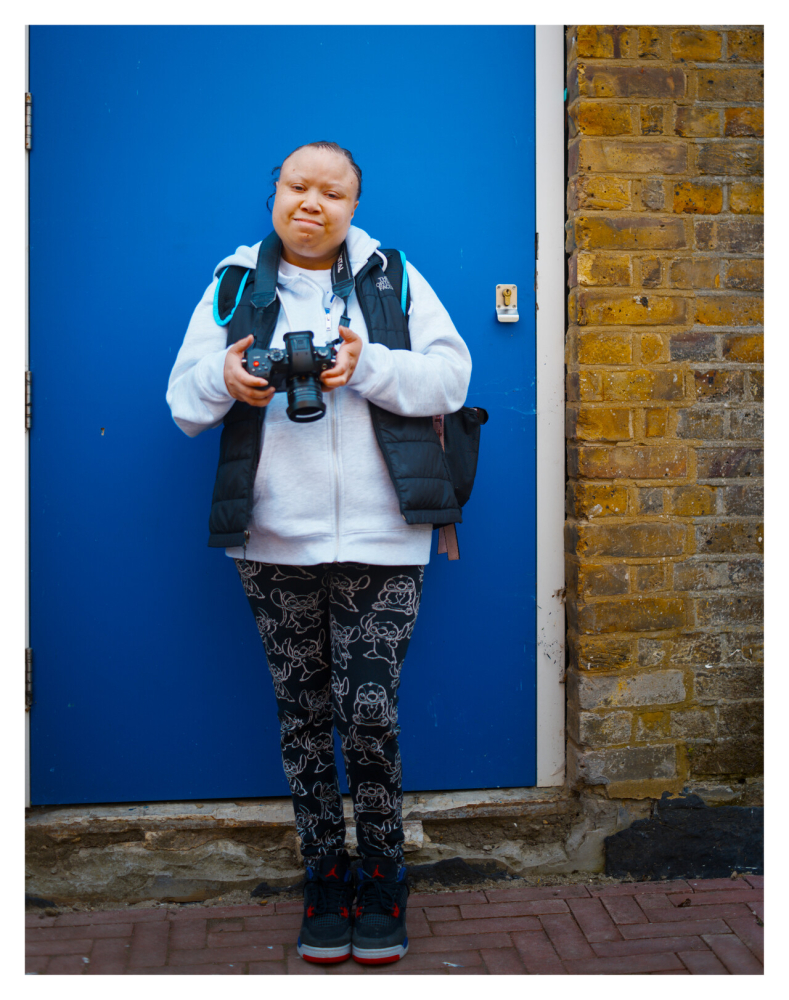 A lady stands holding a camera in front of a blue door