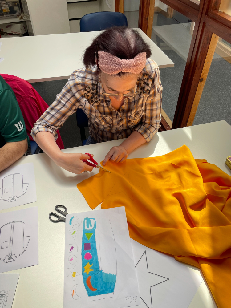 A lady sits at a table cutting some orange fabric