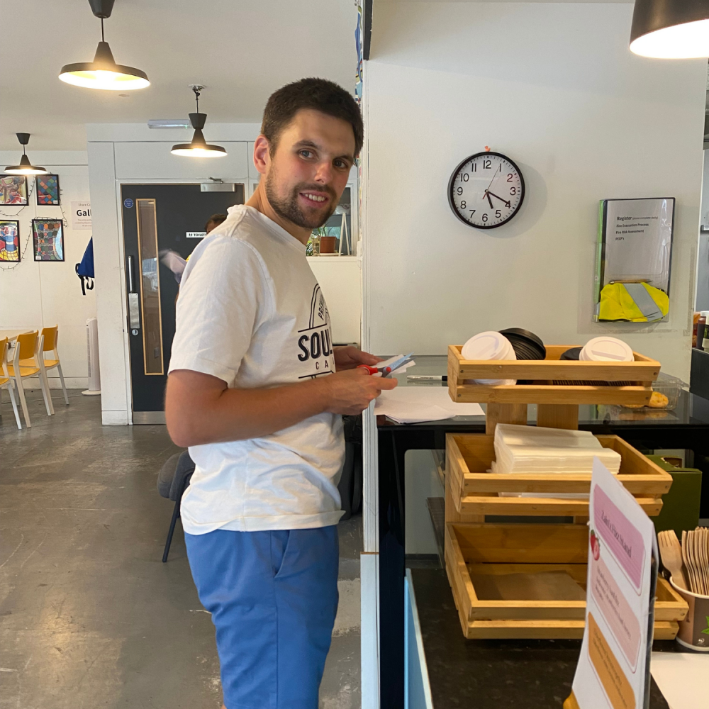 A young man stands smiling before a counter, he's getting everything ready for the supper club