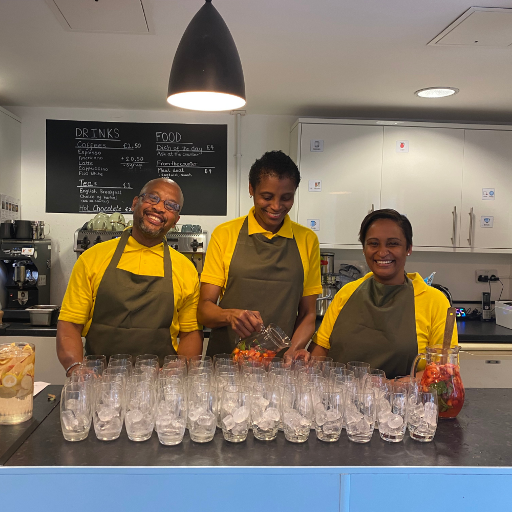 Three people smile at the camera behind a counter full of empty glasses lined up to service mocktails