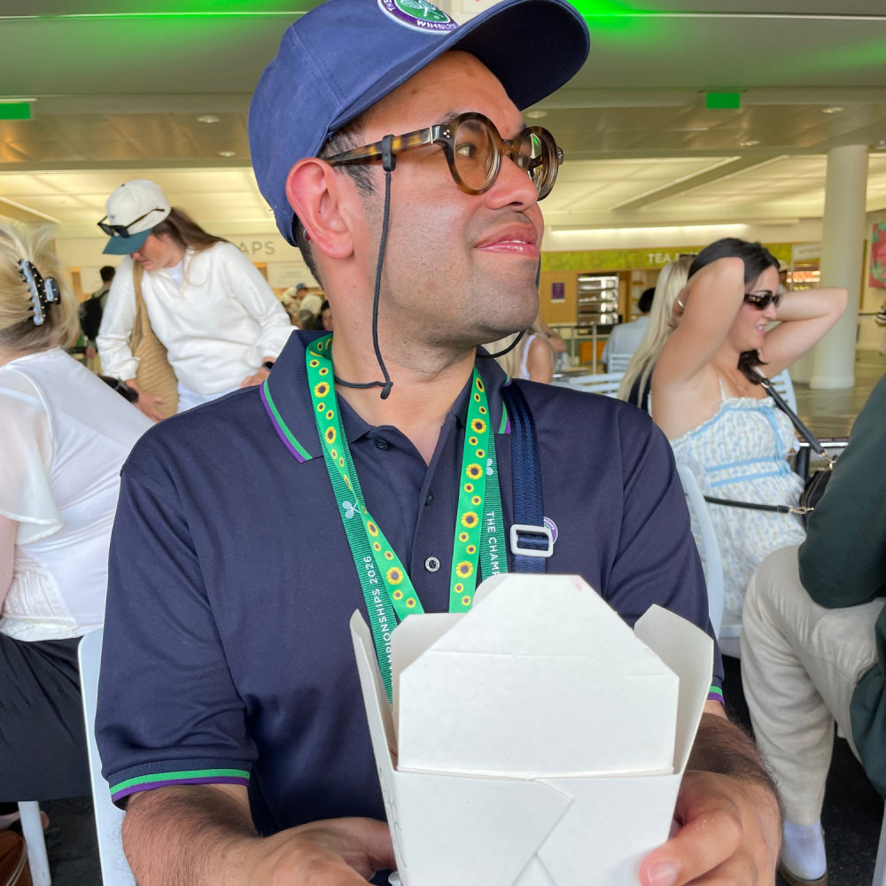 A man looks to the side in a Wimbledon cafe holding a strawberries and cream carton, he's in his work uniform