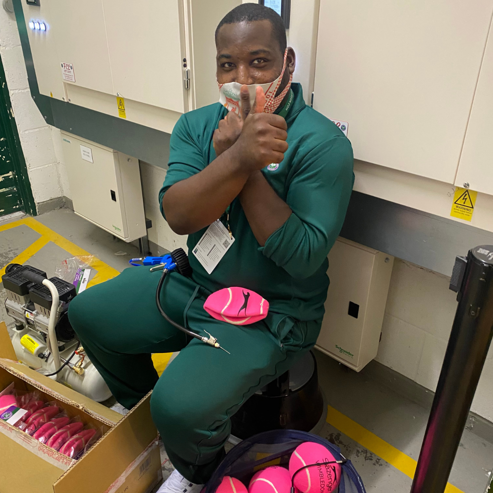 A man sits in his work uniform in the back of a Wimbledon shop and is bagging up and sorting through pink tennis balls