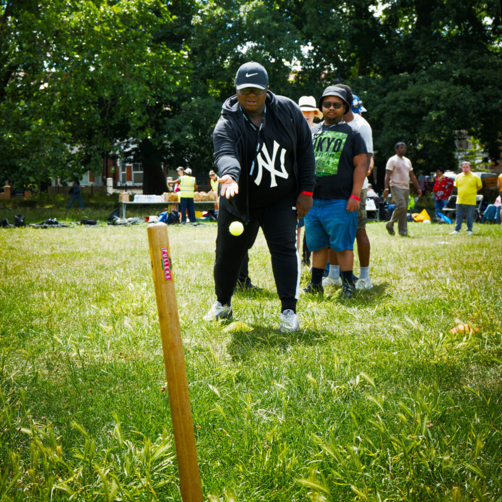 A line of students stand in front of a wooden stick in the ground, trying to hit it with a ball