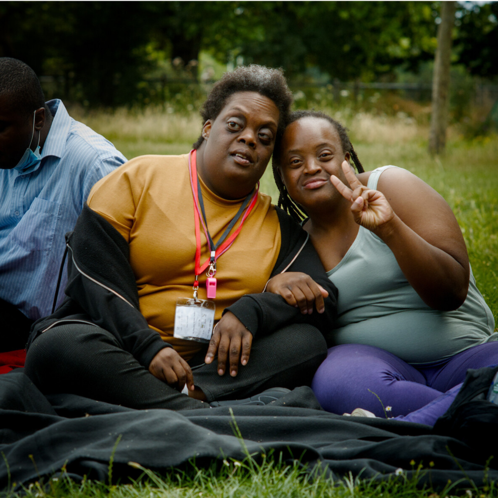 Two women sit on the grass and pose for a photo
