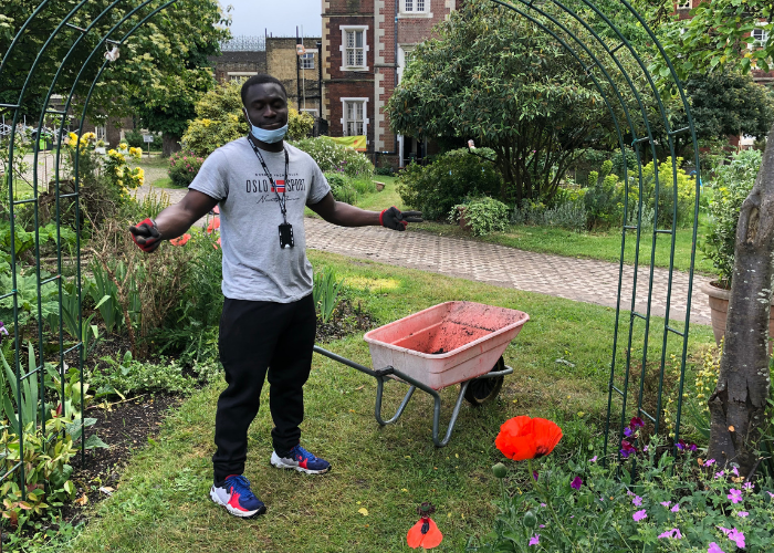 Maxwell standing in the Garden with his wheelbarrow, looking happy