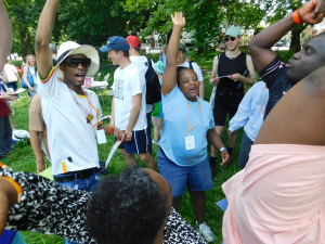 A group of young people who are students at Share stand with their arms up in a park singing and whooping happily at a fun event
