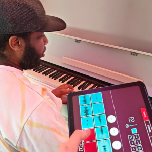 A man sits and plays at a keyboard, next to him a digital app to sample sounds