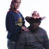 Woman with a hat stands behind a seated male adult who is wearing a handmade stetson style hat