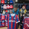 A student at Share is smiling and holding up a Crystal Palace FC football shirt that is for sale