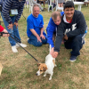3 adults kneel down on the grass to pet a small dog that is on a lead, the owner is out of shot