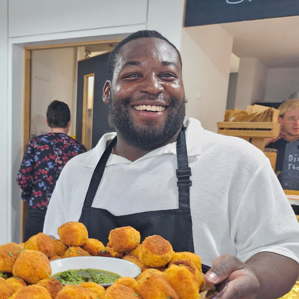 A man stands smiling with a serving platter of food he's just prepared.