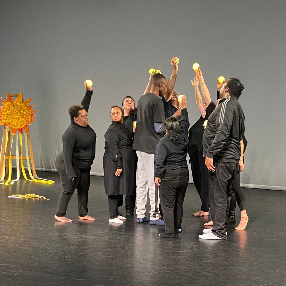 A group of dancers on stage hold up lit bulbs to represent the sun