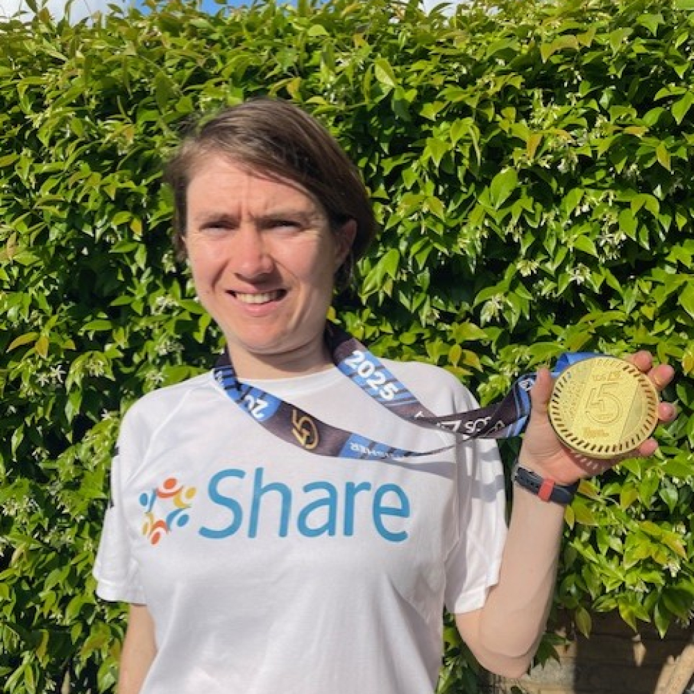 Student Georgia stands in a Share running shirt, proudly holding her medal