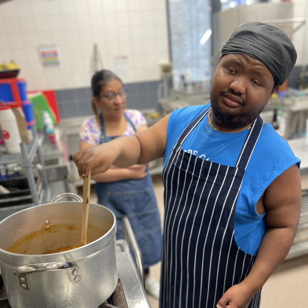 A Share student wearing an apron and stirring a pot with a wooden spoon.