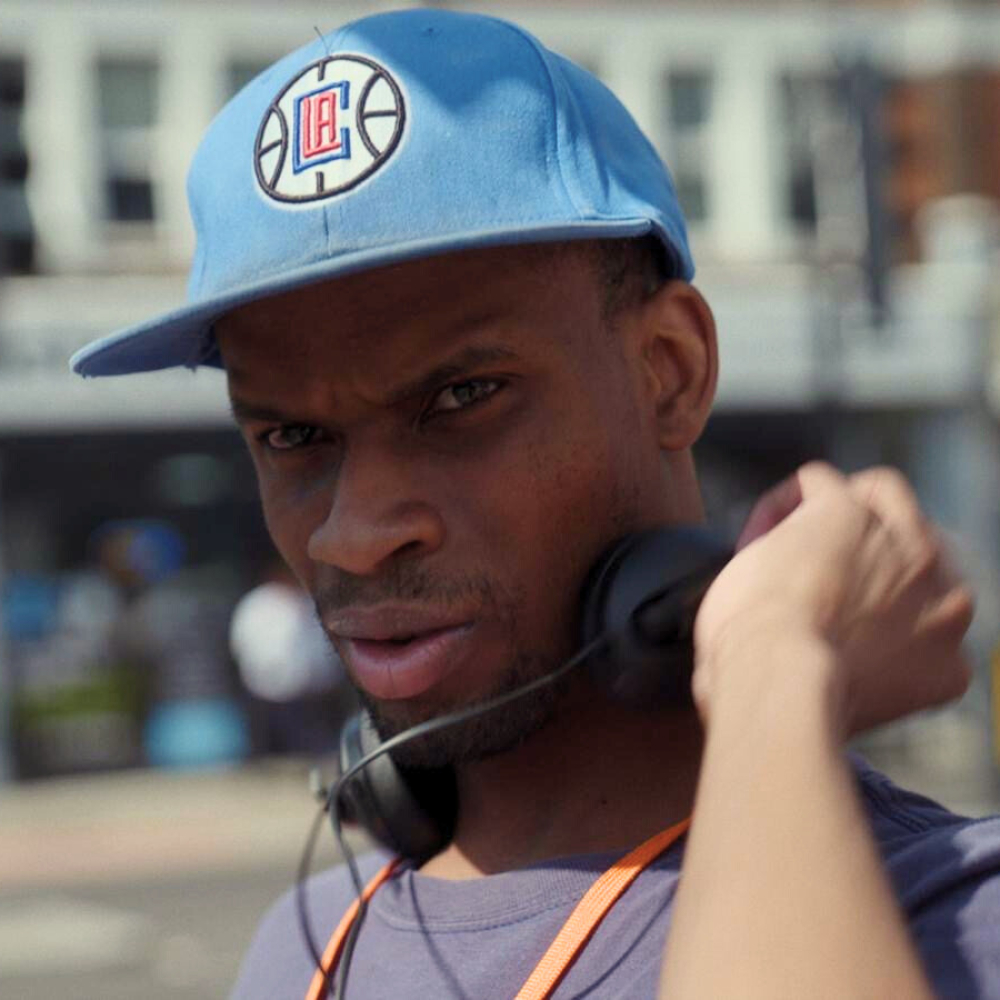 Close up of a young man walking along the street with a baseball cap and headphones around his neck.
