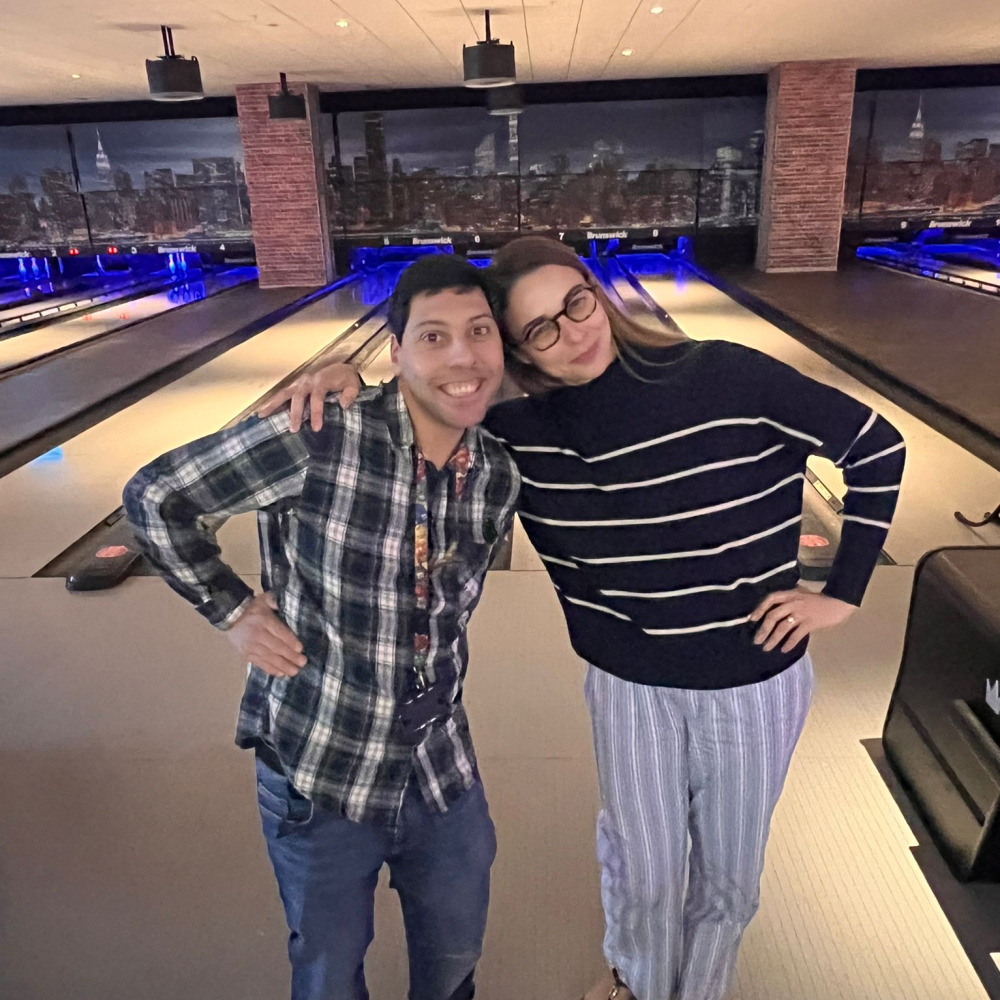 A student and a volunteer stand arm in arm in front of a bowling lane