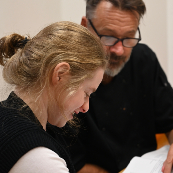 A lady sits looking at some papers on a desk with a member of staff guiding her through