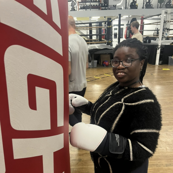 A lady stands with boxing gloves on in a boxing gym.