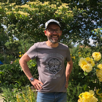 Man smiling next to a yellow rosebush