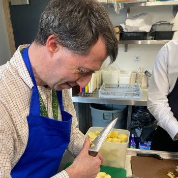 A man in a kitchen peels vegetables.