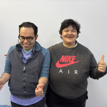 A man and a lady, both students at Share smile and give a thumbs up to the camera