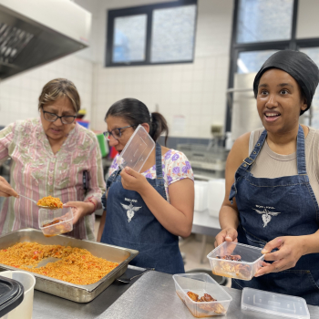 Three ladies wearing aprons get cooking in a catering kitchen