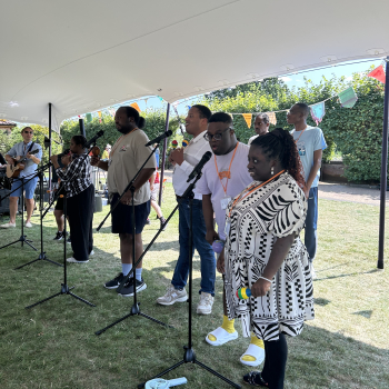Students stand next to microphones under a marquee singing