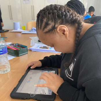 A lady leans over an ipad intently, she's in a classroom learning about digital skills
