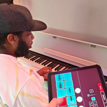 close up of a man sitting at a piano and someone is showing him a digital music app
