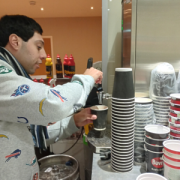 A young man is filling a paper coffee cup at a coffee machine ready to serve a customer