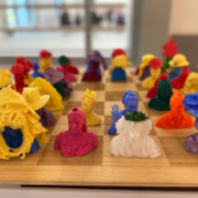 Lots of  multicoloured 3D printed models of people wearing hats, displayed on a chessboard